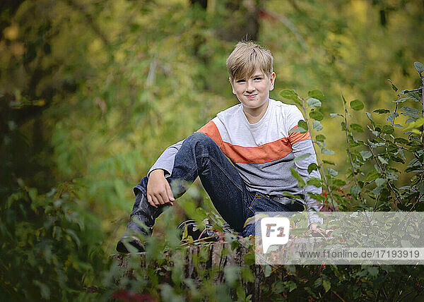 Junger blonder Junge  der draußen in den Bäumen sitzt