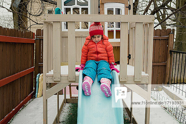 Kind spielt auf der Rutsche an einem kalten  verschneiten Wintertag