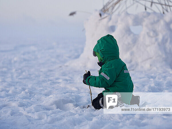 Kleiner Junge spielt mit Stock im Schnee an einem kalten Wintertag