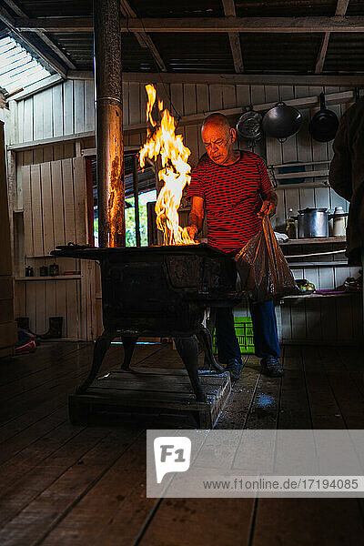 Ein älterer Mann legt Brennholz zum Kochen in die Küche