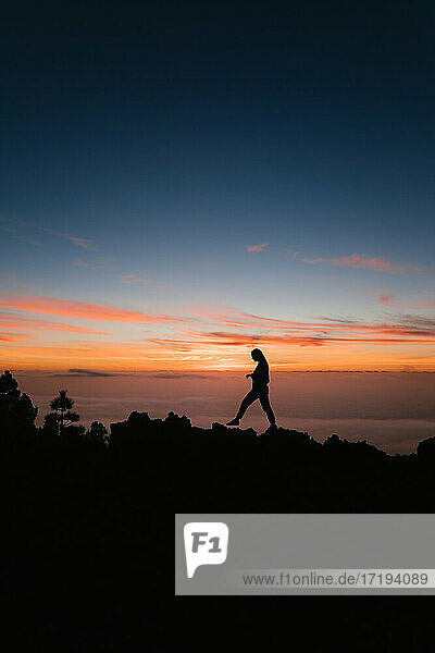 Women walking on rock at cliff against sky during sunset