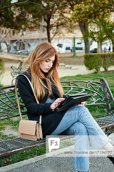 Eine attraktive junge Frau schaut in einem Park auf ihr Tablet
