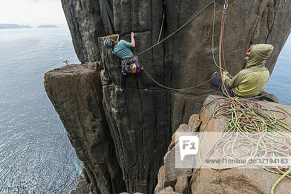 Ein abenteuerlustiges Paar klettert auf den ausgesetzten Felspfeilern von Cape Raoul  wobei die Frau zwei Seile als Schutz benutzt  während sie versucht  einen Weg nach oben zu finden  und der Mann sie in Tasmanien  Australien  sichert.