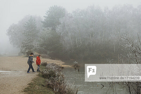 Two brothers standing beside frozen lake in winter against foggy sky