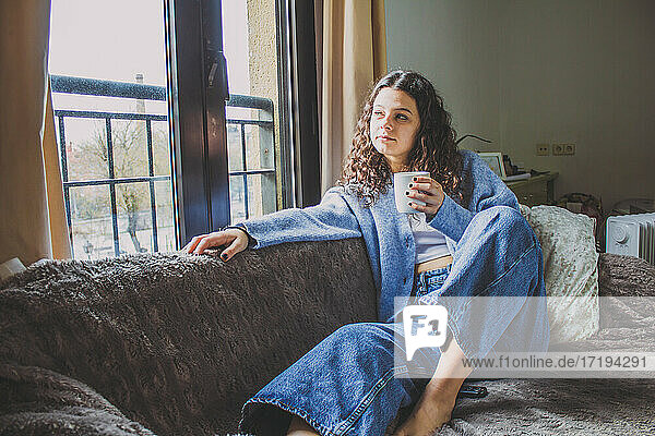 junge Frau beim Frühstück auf dem Sofa mit einem Kaffee