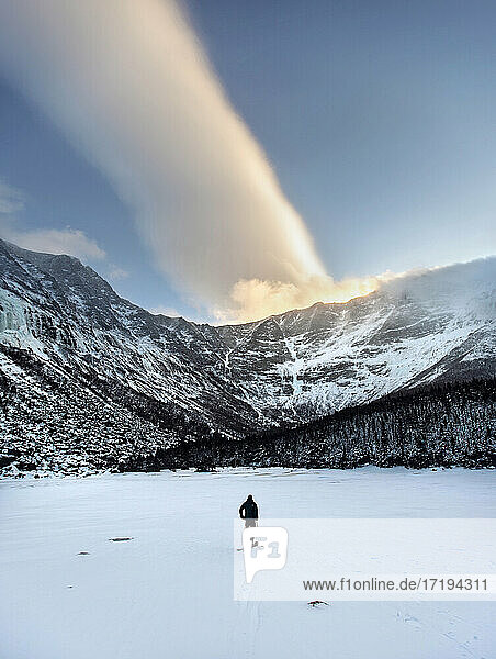 Skier stands on frozen Chimney Pond  Katahdin with unique cloud.