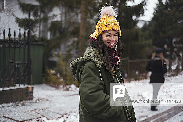 Happy Asian woman with yellow fluffy beanie smiles in snowy street