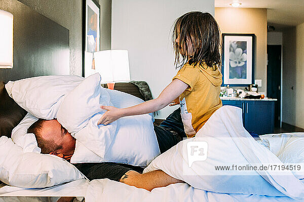 Happy young child playing with father on a bed in a hotel room