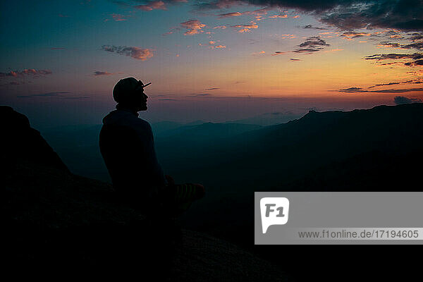 Ein Mann starrt in den Sonnenuntergang auf dem Gipfel eines Berges