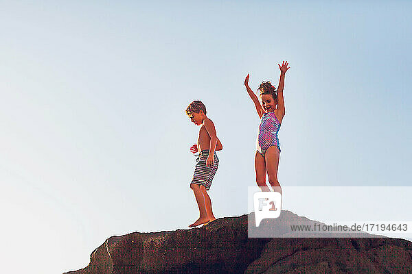 Ein Junge und ein Mädchen klettern auf einen Felsen am Strand.