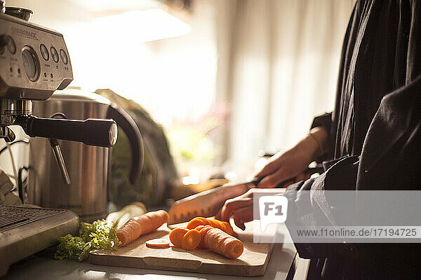 Frau schneidet zu Hause Karotten  um während des Einschlusses ein gesundes Abendessen zuzubereiten