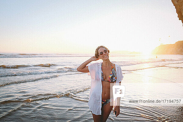 Frau im tropischen Bikini am Strand bei Sonnenuntergang
