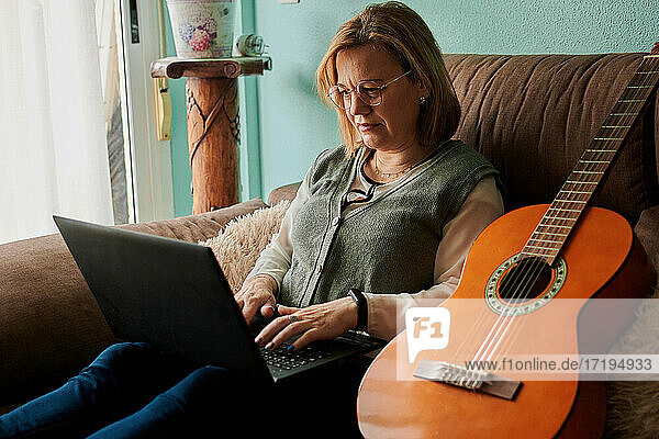 Middle-aged woman learn to play the guitar with a laptop at home