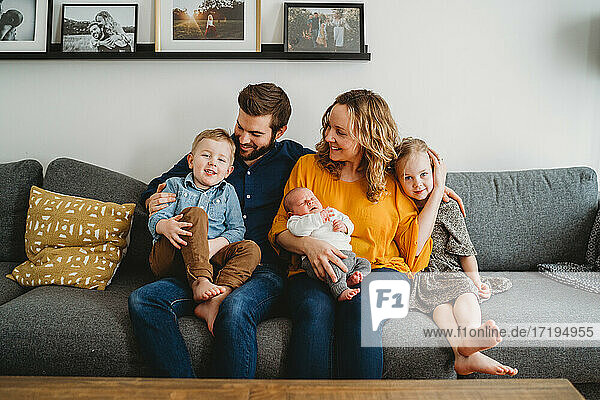 Good looking happy white family holding newborn baby on couch at home