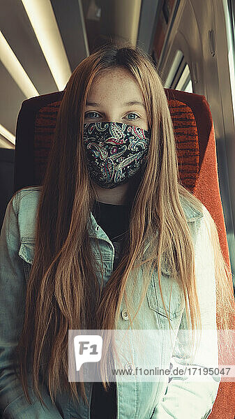 glückliches Mädchen in einem Transportmittel  das eine Maske trägt und in die Kamera schaut