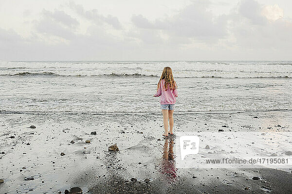 Young girl standing at the waters edge at the beach during dusk