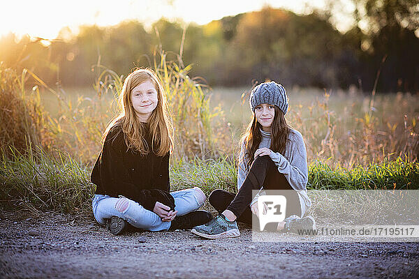 Zwei hübsche junge Mädchen sitzen im Herbst im Freien  im Gegenlicht.