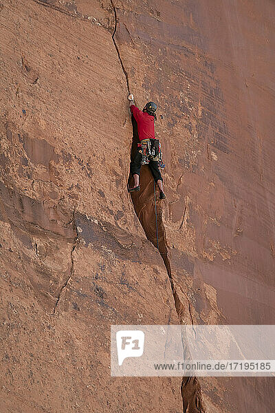 Low angle view of man rocky climbing cliff at Canyonlands National Park