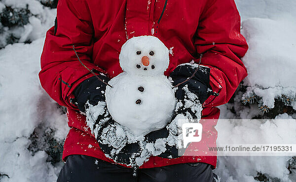 Kind hält an einem verschneiten Tag im Freien einen kleinen Schneemann in den Händen.