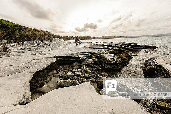 Father and child walking on rocky shore near ocean in New Zealand