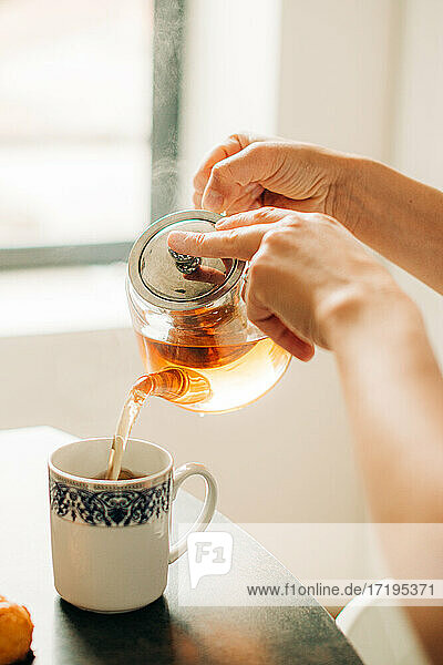 Weibliche Hände gießen heißen Tee in eine Tasse