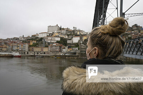 Ein Tourist trägt eine Gesichtsmaske und bewundert die Brücke Dom Luis I und den Fluss Douro