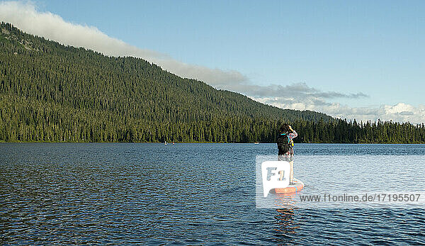 Female paddle boarding on lake near mountain slope and green forest