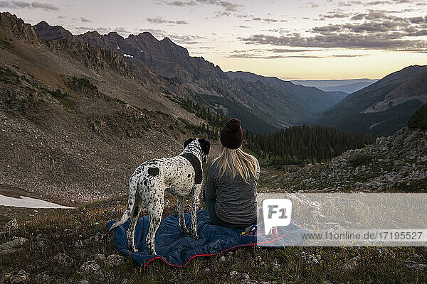 Frau betrachtet die Berge beim Wandern mit Hund bei Sonnenuntergang