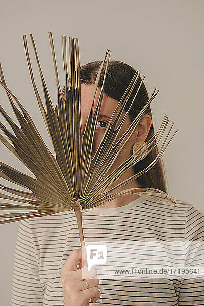 Porträt einer Frau  die durch ein Palmenblatt schaut. Junge Kaukasierin