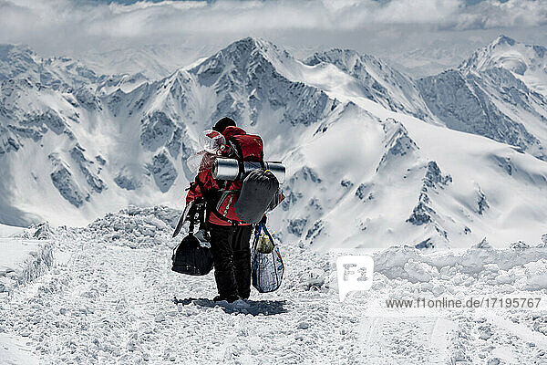 Rückansicht eines männlichen Wanderers  der Taschen trägt  während er auf einem verschneiten Berg im Urlaub wandert