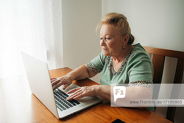 Ältere Frau arbeitet am Computer  während sie zu Hause am Tisch sitzt