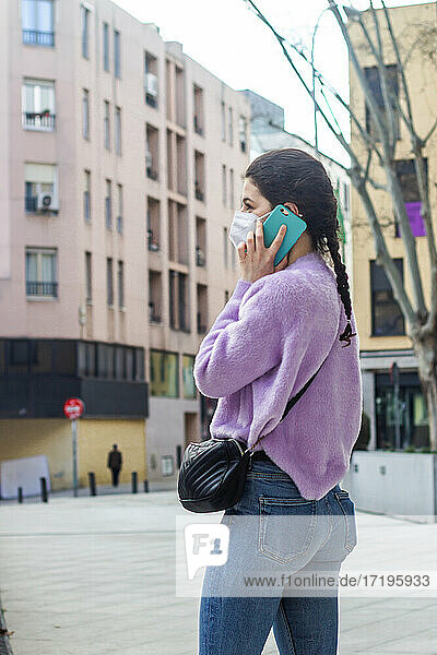 junge Frau mit KN95-Schutzmaske auf der Straße  die mit dem Handy spricht