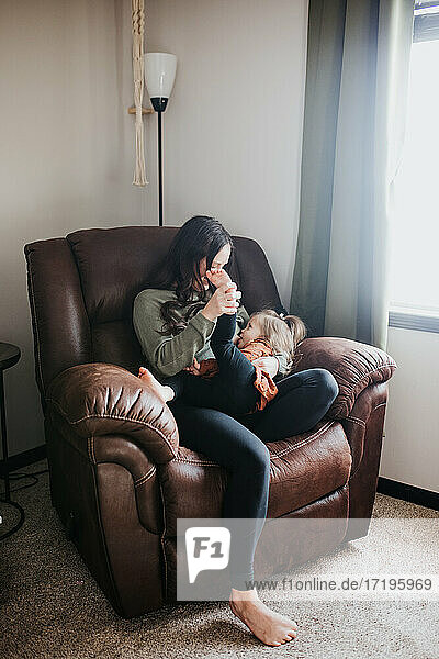 Mother breastfeeding toddler daughter in their home nursery