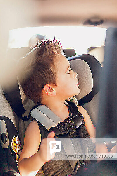 Preschool age boy sitting in car seat inside a car.