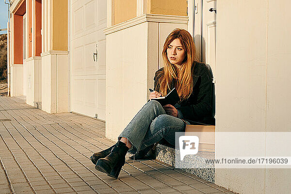 Junge Frau schreibt in ihr Notizbuch  während sie auf der Straße sitzt