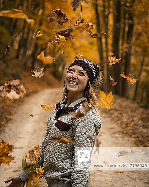 Fröhliche junge Frau  die Herbstblätter wirft  während sie ihren Urlaub im Wald genießt