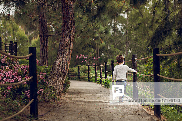 Boy walking down a path next to a rope rail.