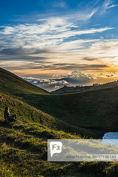 Unbekannte Frau sitzt im Gras und sieht den Sonnenuntergang auf dem Berggipfel