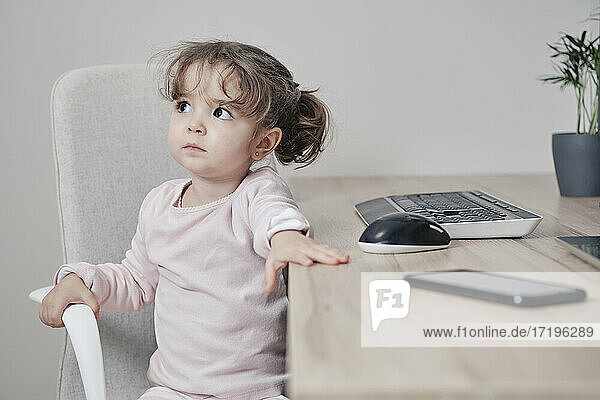 Ein 2-jähriges Mädchen sitzt auf einem Bürostuhl mit einer Tastatur  einer Maus