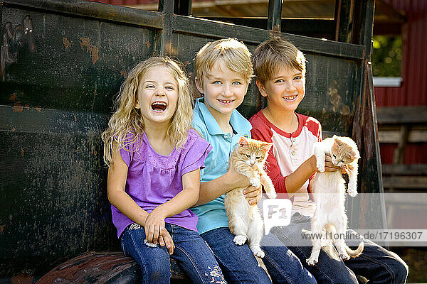 Drei glückliche blonde Kinder spielen mit Kätzchen im Freien.