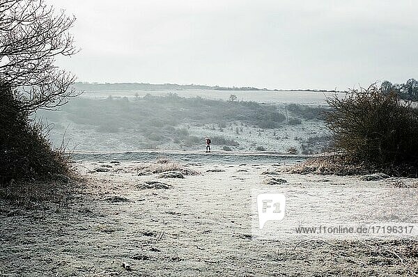 Frau  die auf einem frostigen Weg in der englischen Landschaft im Winter spazieren geht