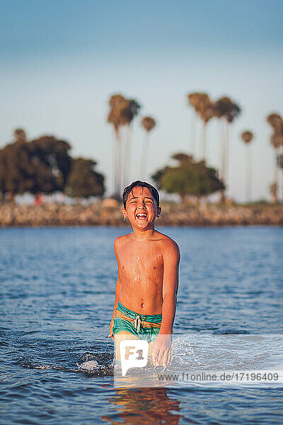 Lächelnder Junge  der auf dem Wasser in Richtung der Kamera läuft.