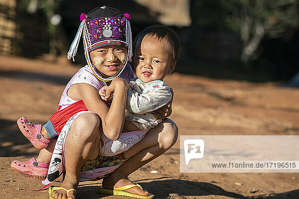 Young boy and his baby brother of Akha tribe kneeling on ground  near Kengtung  Myanmar
