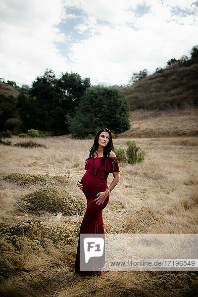 Werdende Mutter posiert im Feld im roten Kleid in San Diego