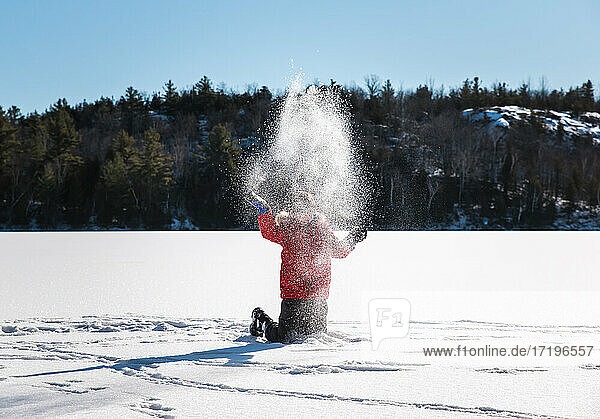 Junge wirft Schnee in die Luft in der Mitte eines zugefrorenen Sees.