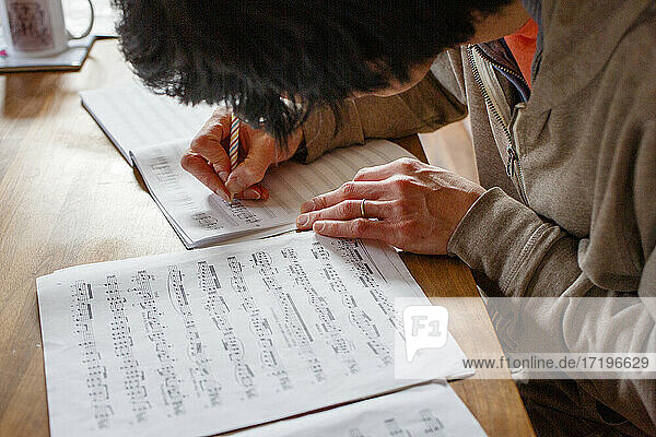 Ein Mann sitzt an einem Holztisch und schreibt mit einem Bleistift Noten ab.