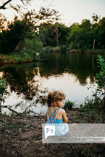 Junges Mädchen sitzt am Bachufer bei Sonnenuntergang im Sommer