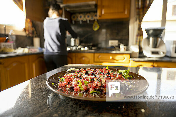 Nahaufnahme eines Granatapfelsalats auf dem Tisch  während eine unkonzentrierte Frau in der Küche kocht