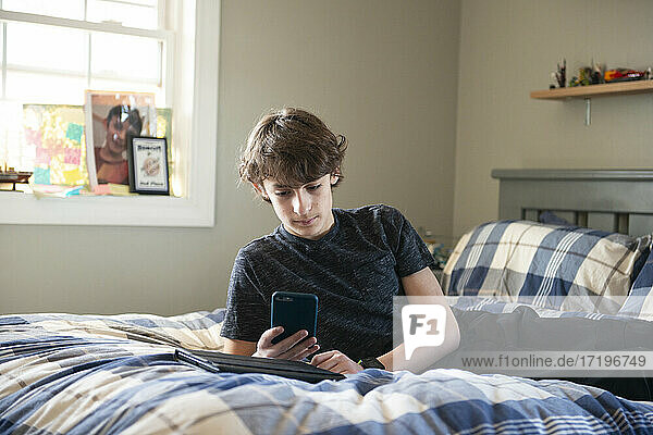 Kleiner Junge auf dem Bett mit Telefon und Tablet.