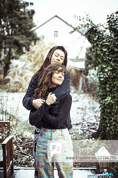 Queer weiblichen Paar umarmen und lächeln  während Schnee fällt in Hinterhof
